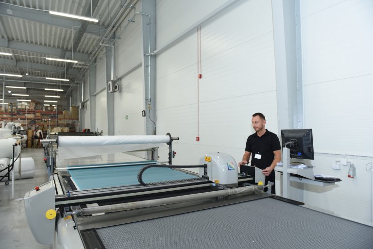 Polaszek Meble Pracownik obsługujący dużą maszynę do krojenia tkanin w warunkach przemysłowych, specjalizujący się w Meble na zamówienie. Chojnice