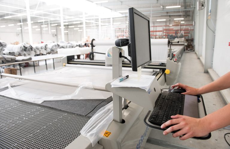 Polaszek Meble Osoba obsługuje komputer przy przenośniku taśmowym w przemysłowej krojowni specjalizującej się w produktach Meble Polaszek. Chojnice